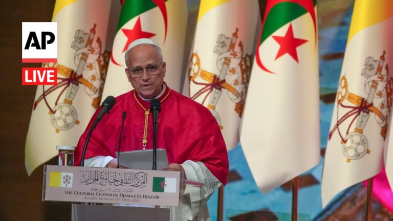 Religious leader in red robes delivering a speech at a podium, with Algerian flags in the background and an AP Live logo.