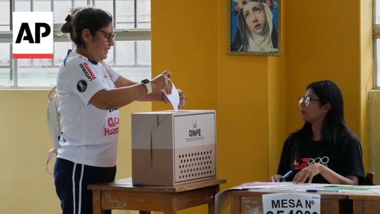 Voter deposits ballot into ONPE ballot box as an election official sits at a desk in a yellow-walled room.