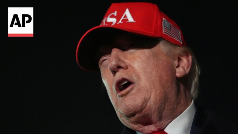 AP news photo: close-up of a man wearing a red cap with 'USA' on it, speaking with mouth open against a dark background, AP logo visible in the corner.