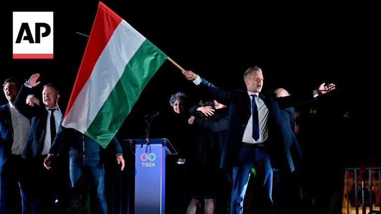 Politicians celebrate on stage at night, waving a Hungarian flag; AP News logo visible to the left.
