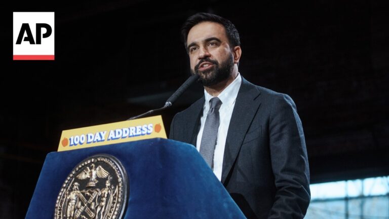 Male speaker in a dark suit delivers a speech at a podium labeled '100 Day Address' with an AP logo visible in the top left.
