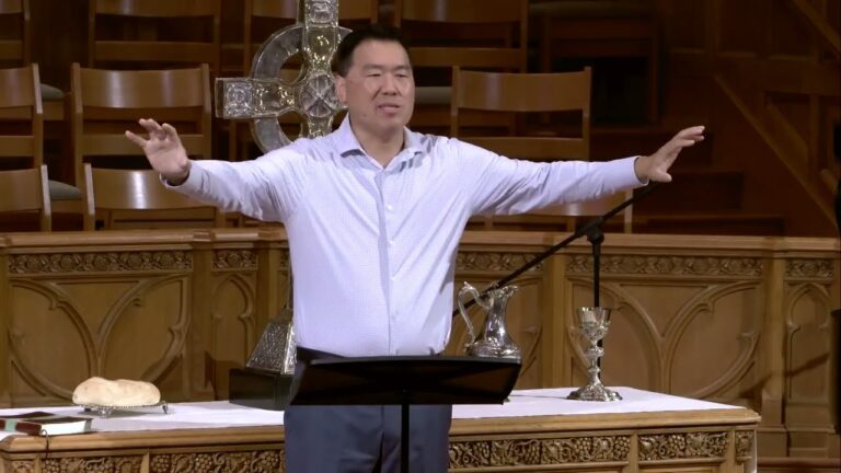 Pastor standing at the altar with arms extended, delivering a sermon in a church.
