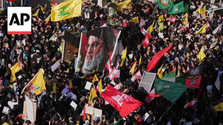 Dense protest crowd waving yellow, green, and red flags with numerous banners and a large portrait banner in the center, AP logo visible in the corner