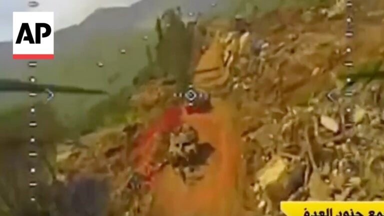 Drone view of a rocky hillside with debris and a dirt road below, from a news broadcast (AP logo).