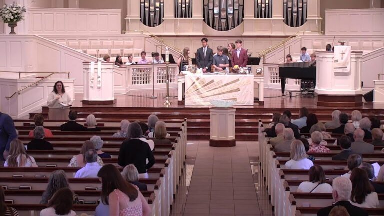 Ceremony in a church sanctuary with people at a podium on stage and organ pipes in the background, audience seated in pews.