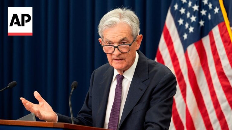 Older man in a dark suit and glasses speaks at a podium with microphones, AP logo in the corner and the US flag behind him in a press briefing.