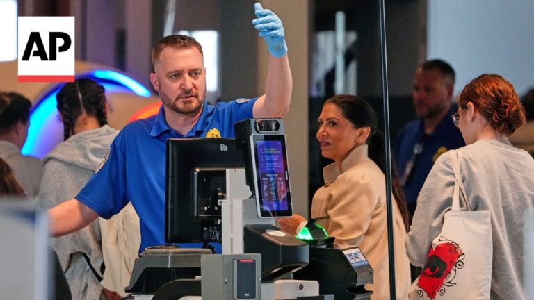 AP photo: man in a blue uniform raises a gloved hand beside a self-checkout kiosk while a woman observer looks on.