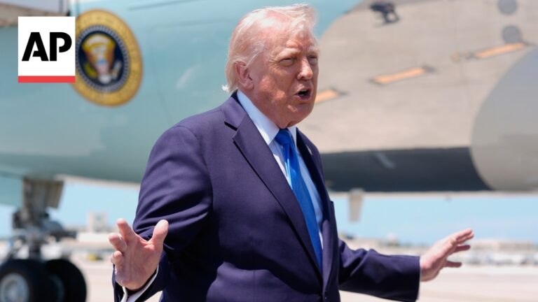 Man in a dark suit and blue tie speaks with his hands outstretched on a tarmac next to a military aircraft; AP logo in the corner.