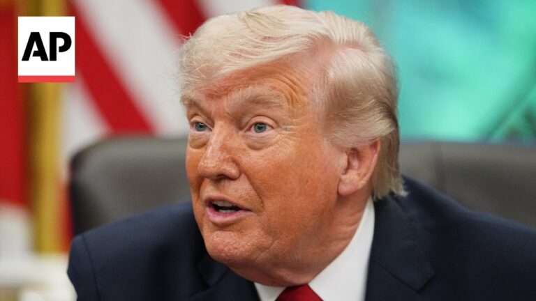 Close-up of a man with light hair in a dark suit and red tie speaking, AP logo in the corner.