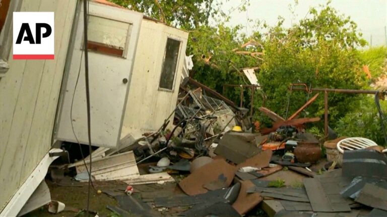 Debris and a tilted small shed in a chaotic outdoor pile of trash and rubble, with greenery in the background (AP watermark).