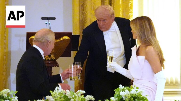 Toast at a formal event: three well-dressed guests raise champagne glasses in a gilded room with an AP logo visible on the left side.