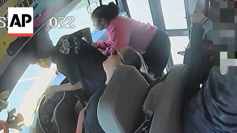 Bus interior with several passengers; a woman in a pink top leans toward the front, others seated nearby, some faces blurred.