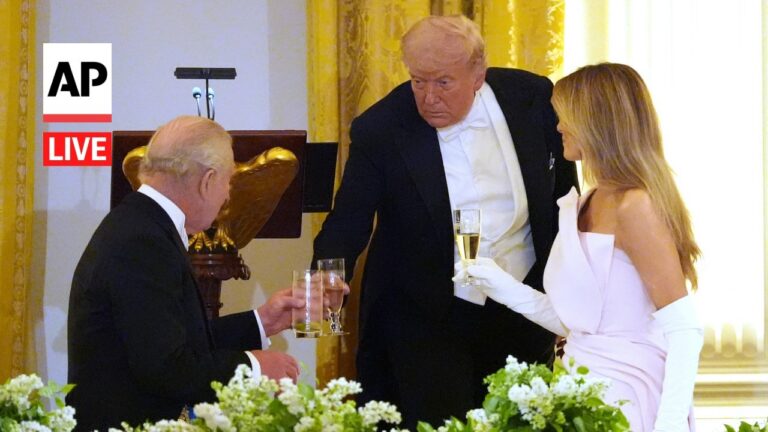 Three people in formal attire toast with champagne at a lavish reception, gold drapes and floral centerpiece in the foreground, AP Live logo on the left.