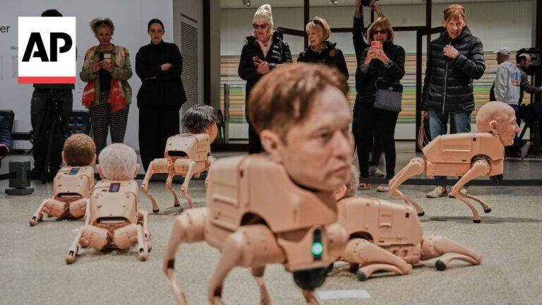 Audience watches beige bipedal robots crawling on a museum floor during a tech demo, with the AP logo visible on the left.