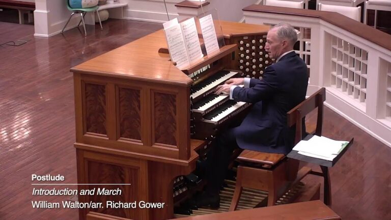 Organist playing a wooden pipe organ, reading sheet music during a postlude performance in a church setting.