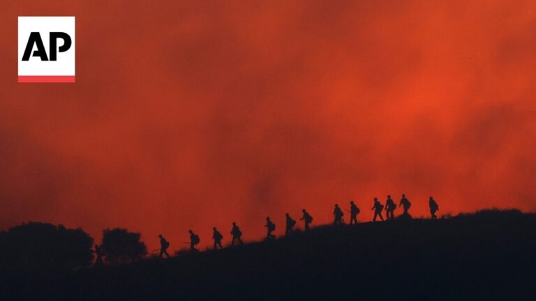 Group of hikers silhouetted along a hillside at sunset with a vivid red-orange sky; AP logo in the top-left corner.