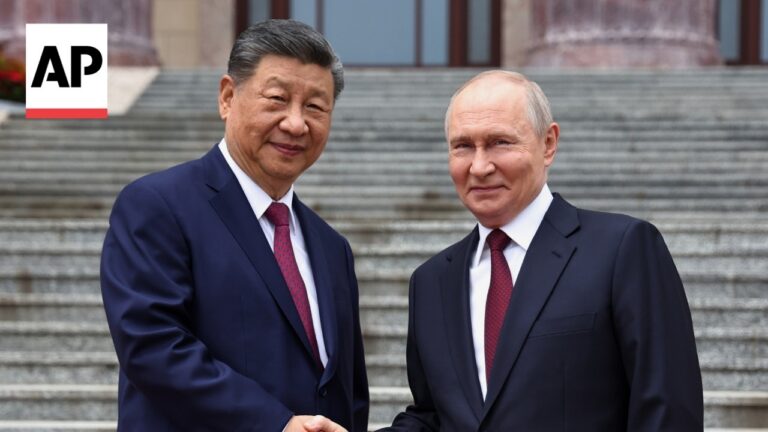 Two men in dark suits shaking hands on stone steps outside a building, with an AP news logo in the top-left corner.