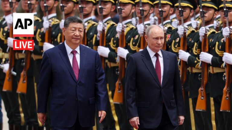 Two men in dark suits walk side by side as a ceremonial guard in formal uniforms stands behind, AP Live watermark visible on the left.