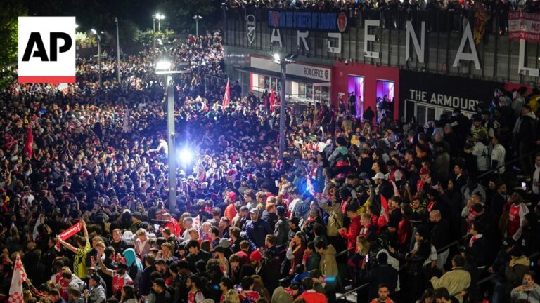 Nighttime scene of a packed stadium concourse with thousands of sports fans, many in red and white, under bright lights and banners.