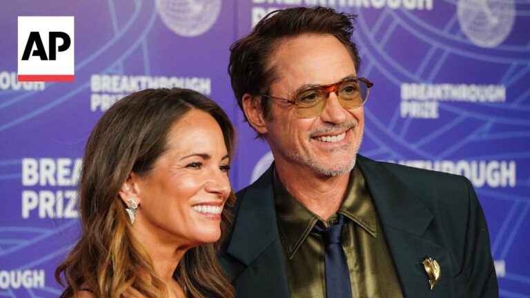 Two smiling guests posing at a Breakthrough Prize event against a purple backdrop with an AP logo nearby.