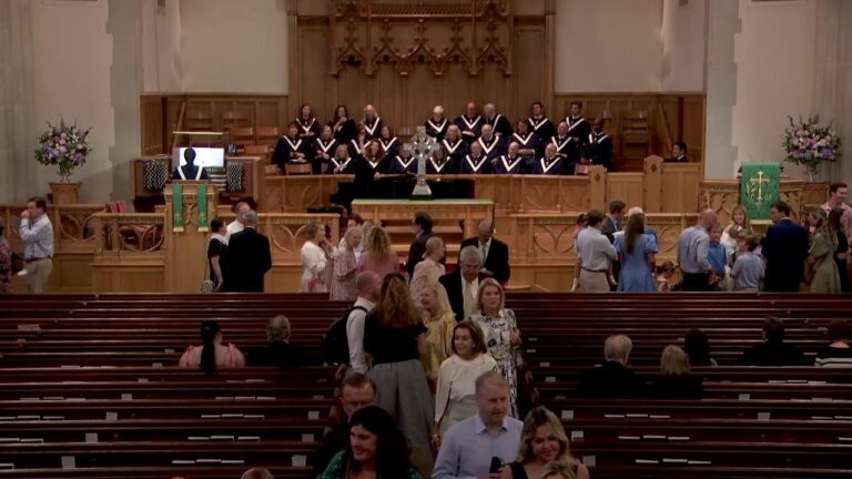 Choir in matching robes stands on a wooden platform behind a raised altar inside a church.