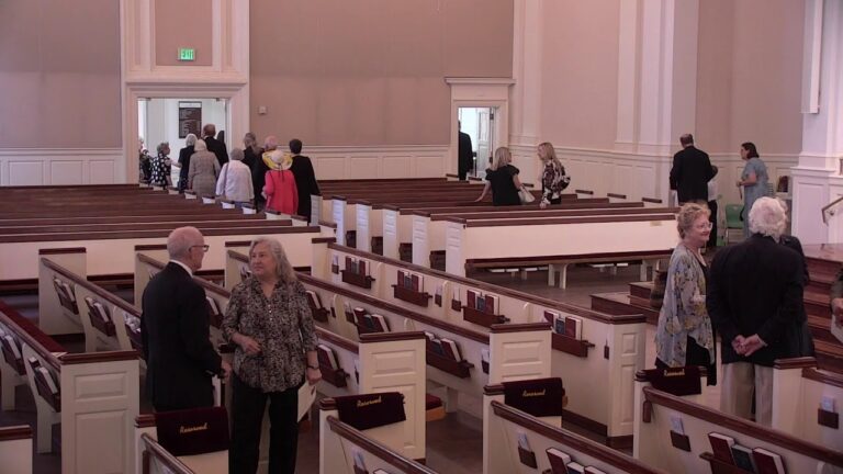 Group of seniors touring a church interior with wooden pews and white paneled walls in a spacious sanctuary.
