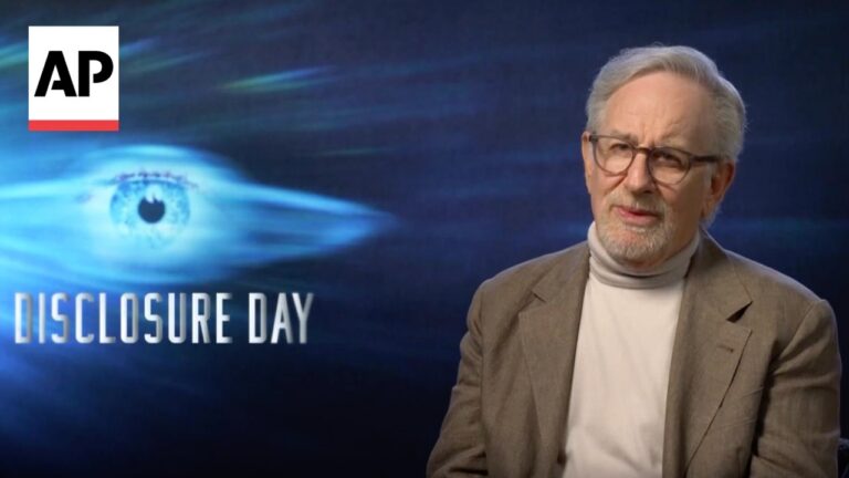 AP logo in the upper left; older man with glasses in a beige blazer and light turtleneck speaks on a blue backdrop reading “Disclosure Day.”