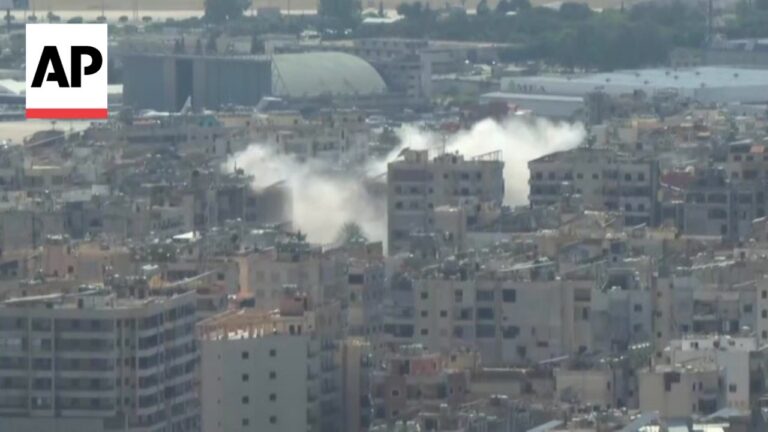 Aerial view of a crowded urban area with smoke plumes rising from several buildings, AP logo in the corner indicating news footage.