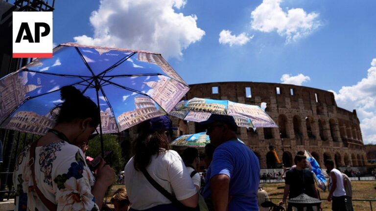AP logo in the corner as people hold souvenir umbrellas near the Colosseum in Rome on a sunny day