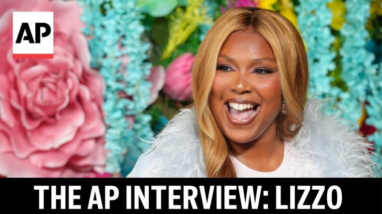 Lizzo laughing with mouth open in a white fluffy coat, colorful flower backdrop; AP logo in the top-left corner.