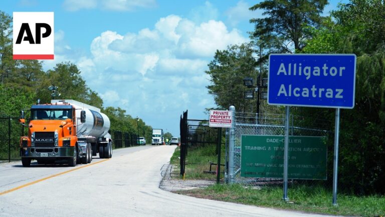 AP logo in the upper left; an orange Mack tanker truck drives along a rural road toward a blue Alligator Alcatraz sign on the right.