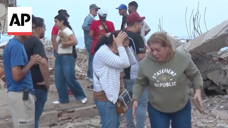 Group of people among rubble at a collapsed building, looking distressed as they assess damage (AP logo on left).