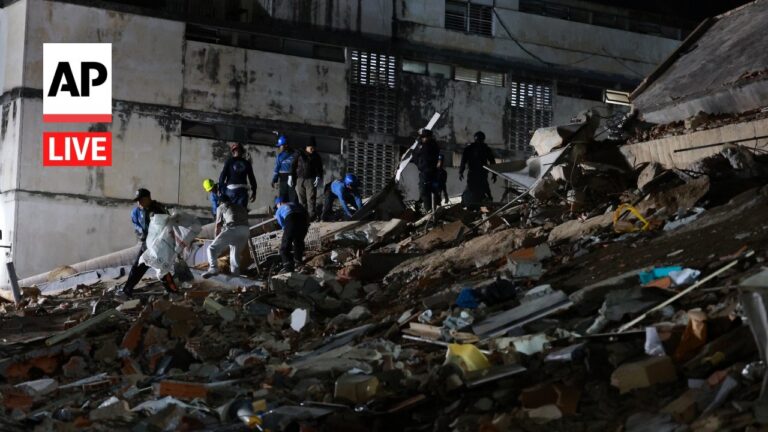 AP Live: rescuers in helmets search through rubble inside a collapsed building.