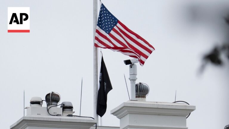 American flag waving on a flagpole atop a white building, AP logo visible in the top-left corner.