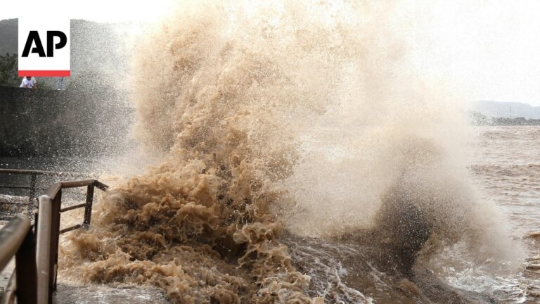 AP logo in top-left; a huge muddy wave crashes over a railing at a waterfront.