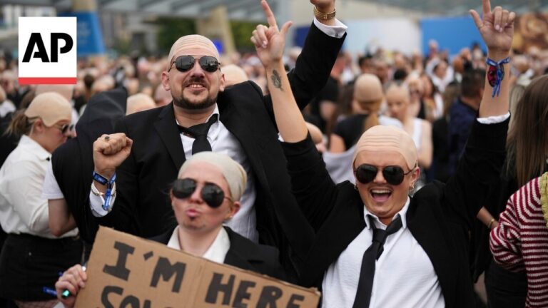 AP logo beside a crowded rally; two bald, suited men raise their arms among cheering attendees with sunglasses on