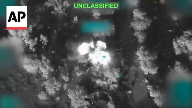 Aerial night-vision image of a forest explosion with a bright blast at center, crosshair targeting marks, and an UNCLASSIFIED label above; AP logo in corner.