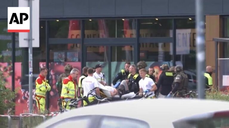 Emergency responders carry a person on a stretcher outside a storefront, AP logo visible in the corner.