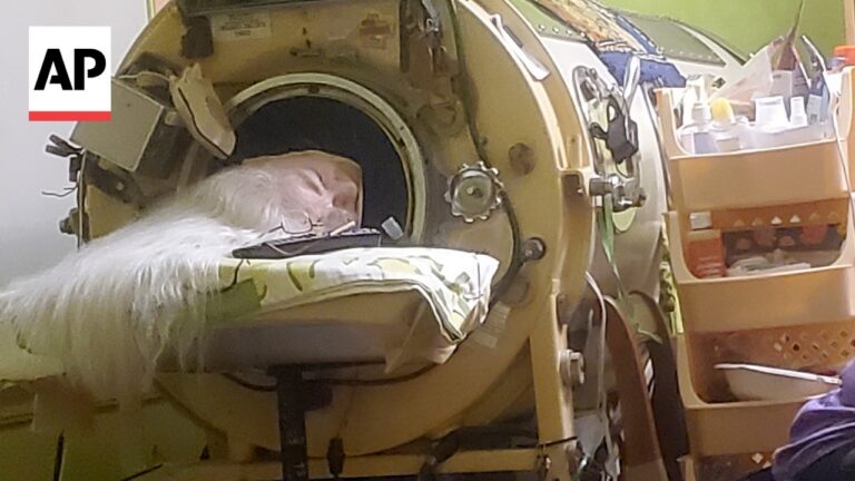 White cat resting inside a round medical scanner chamber with a blanket across the opening, AP logo visible in the corner.