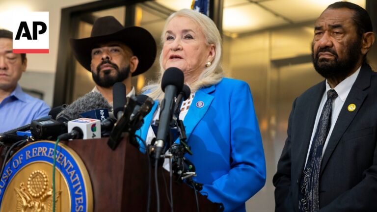 Woman in a bright blue blazer speaks at a press conference from a podium with multiple microphones; AP logo visible in the upper left corner.