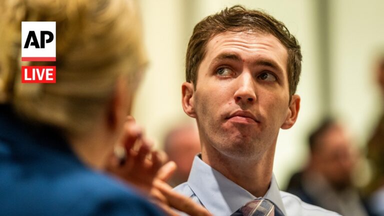 Young man in a dress shirt and tie looks to the side during a press briefing, AP Live logo visible in the corner of the frame.