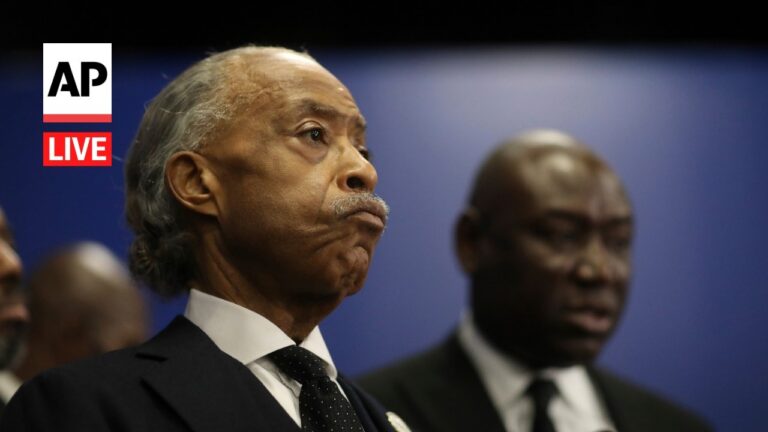 AP Live logo on the left; a gray-haired man in a dark suit makes a pursed-lip expression at a press conference, with two men in suits blurred in the background.