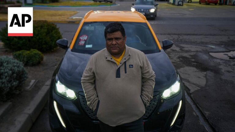 Taxi driver stands with hands in pockets in front of a black taxi with an orange roof and headlights on; AP logo in the corner.