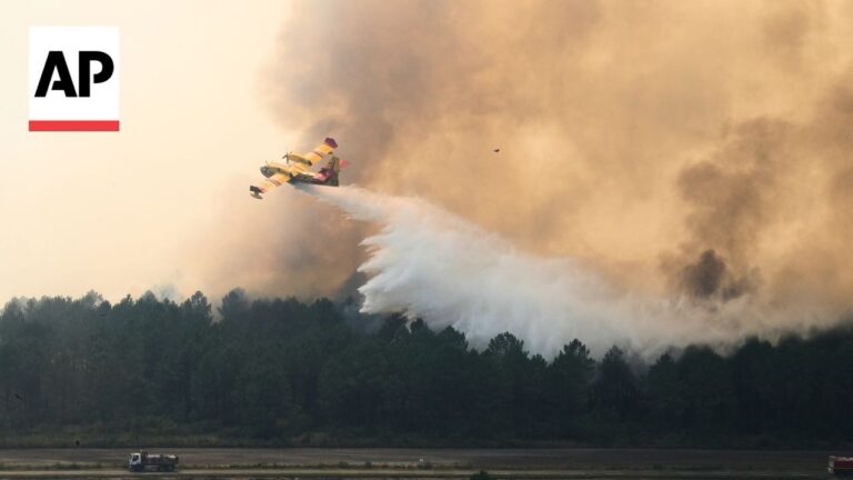 AP logo in top-left; firefighting plane drops water over a forest fire with smoke.