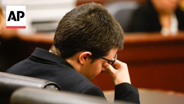 Person wearing glasses sits in a courtroom with head resting on a hand, AP logo in the corner.