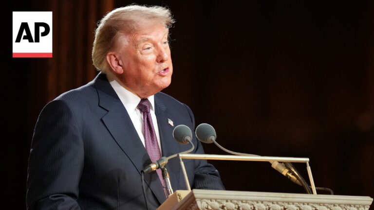 Donald Trump speaking at a lectern with two microphones, wearing a navy suit and red tie, AP logo visible in the corner.