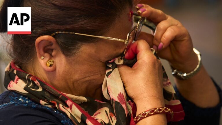 Close-up of a woman adjusting a patterned scarf around her neck and face, wearing glasses, with an AP logo in the corner