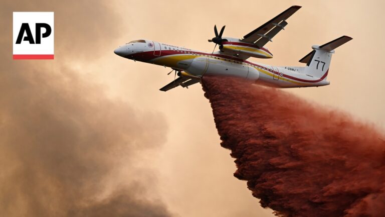 AP photo: firefighting air tanker dispersing red retardant over a wildfire, aircraft in flight with smoke in the background.