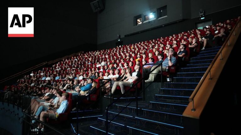 Crowded movie theater audience seated in red chairs, AP logo in the top-left corner