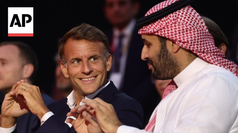 AP logo visible as two men converse at an event: a smiling businessman in a dark suit and a man in a white shirt with a red-and-white keffiyeh.